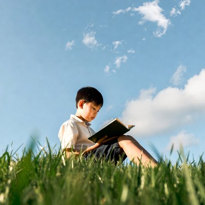 Asian boy reading book on grass