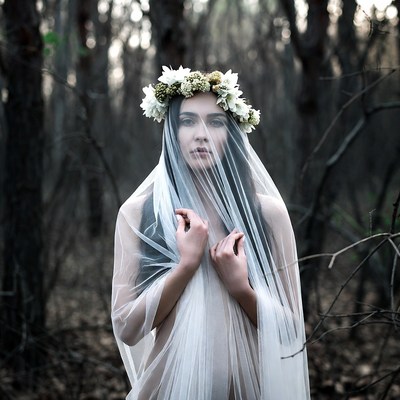 Woman in sheer veil and flower crown in forest