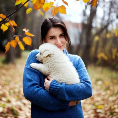 Woman holding fluffy puppy in autumn forest