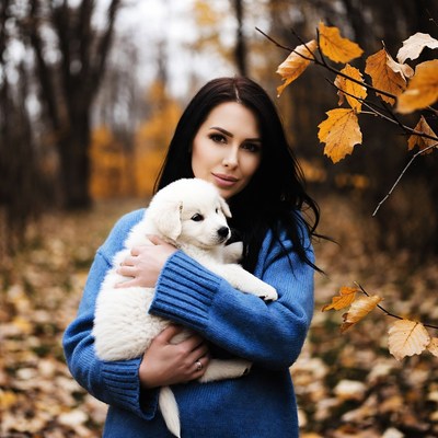 Woman holding white puppy in autumn forest