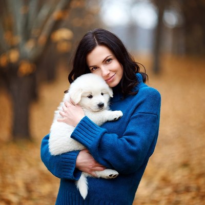 Woman holding white puppy in autumn forest