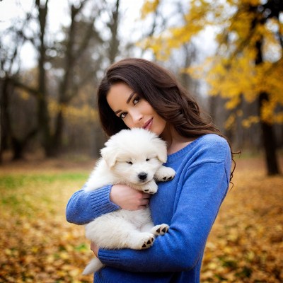 Woman holding white puppy in autumn forest