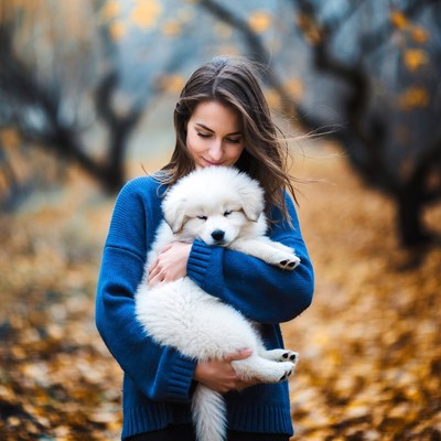 Woman holding white puppy in autumn forest