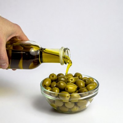 Hand pouring olive oil on olives