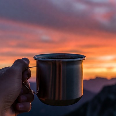Hand holding mug at sunset mountains