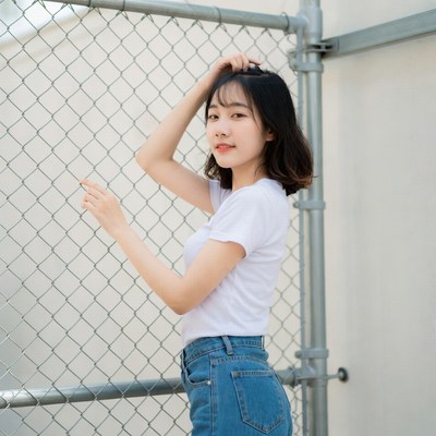 Asian woman posing by chain link fence
