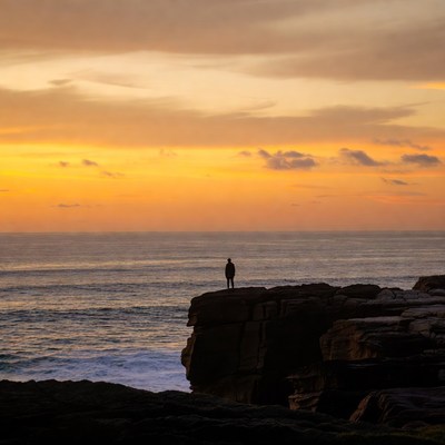 Silhouette man on ocean cliff at sunset