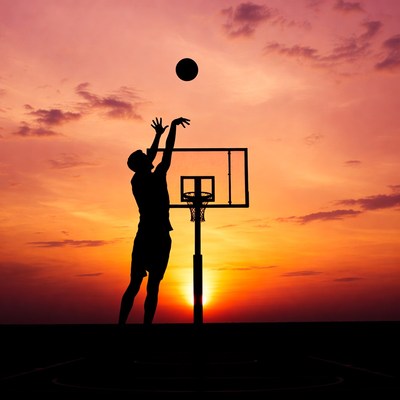 Silhouette man dunking basketball sunset