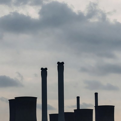 Silhouetted Factory Chimneys Against Cloudy Sky