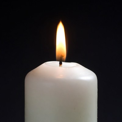 Burning white candle on black background
