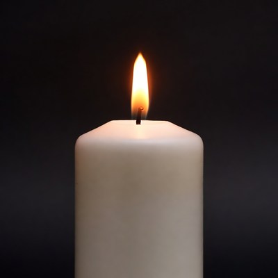 Burning white candle on black background