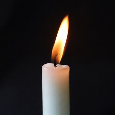 Burning white candle on black background