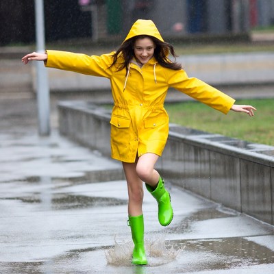Girl jumping in yellow raincoat and green boots