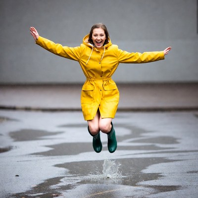 Woman jumping in yellow raincoat and green boots