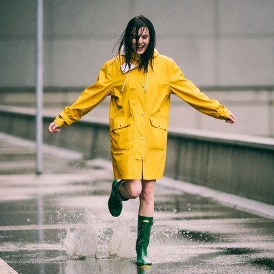 Woman splashing in rain with yellow raincoat