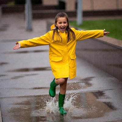 Girl jumping in puddles in yellow raincoat