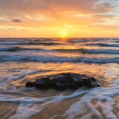 Sunset over ocean waves and rock
