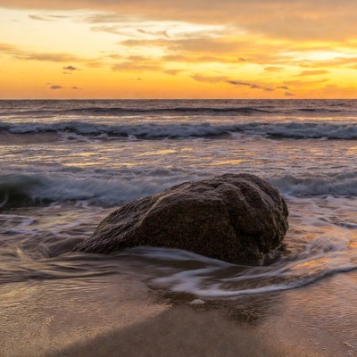 Large rock in ocean waves at sunset
