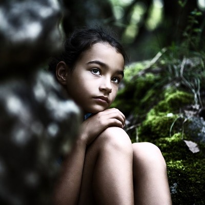 Girl peering from rocks in forest