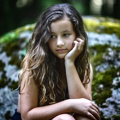 Girl sitting on mossy rock in forest