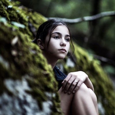 Girl peeking from mossy rock in forest