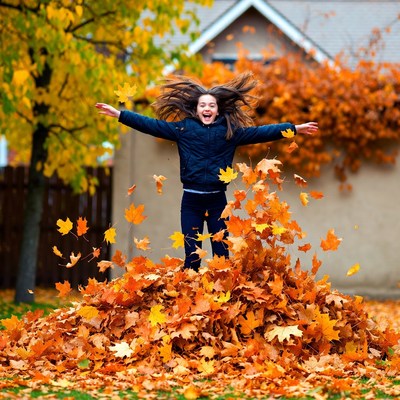 Girl jumping in autumn leaf pile