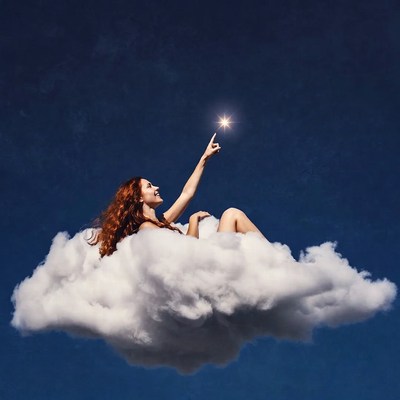 Redhead woman reaching for star on clouds