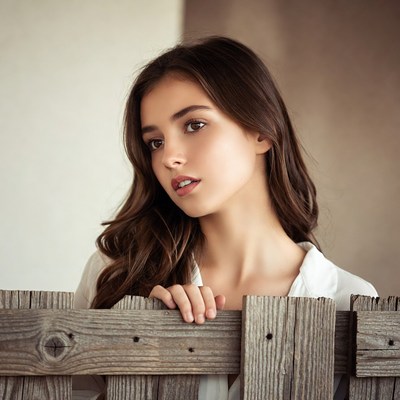 Young woman peeking over wooden fence