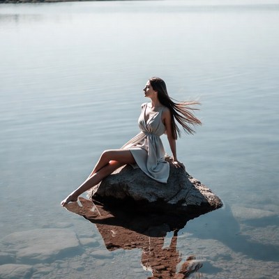 Woman in white dress on lakeside rock