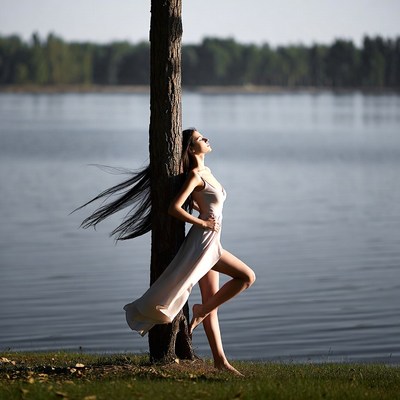 Woman leaning against tree by lake
