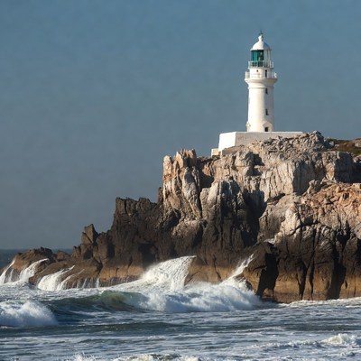 White Lighthouse on Rocky Cliff with Waves