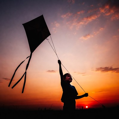 Boy flying kite at sunset silhouette