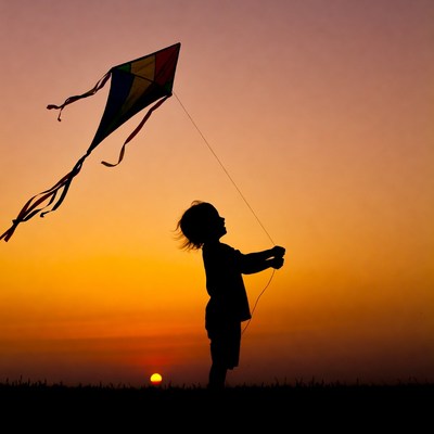 Boy flying kite at sunset silhouette