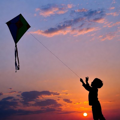 Boy flying kite at sunset silhouette