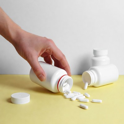 Hand pouring pills from white bottle