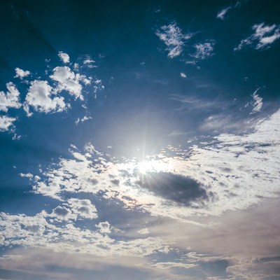 Bright Sun Behind Clouds in Blue Sky