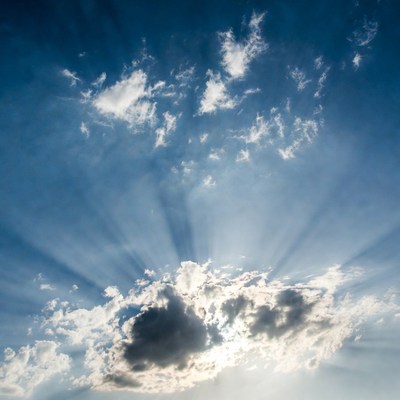 Sun rays through clouds in blue sky