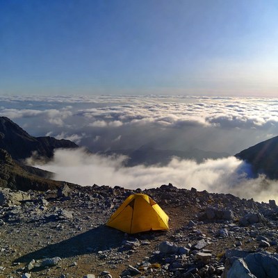 Yellow tent on mountain above clouds