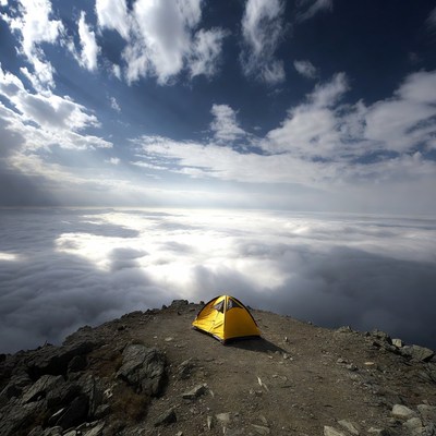 Yellow tent on mountain peak above clouds