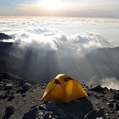 Yellow tent on mountain above clouds