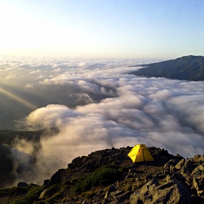 Yellow tent on mountain above clouds