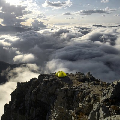 Yellow tent on mountain peak above clouds