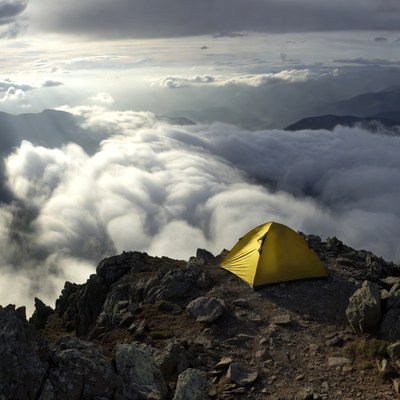Yellow tent on mountain peak above clouds
