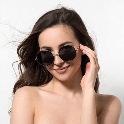 Woman in round sunglasses touching face