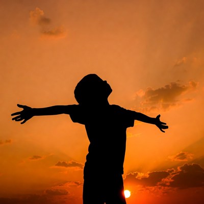 Boy silhouette arms outstretched sunset