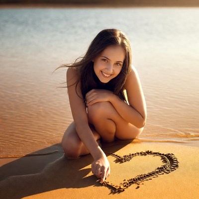 Nude woman drawing heart in sand