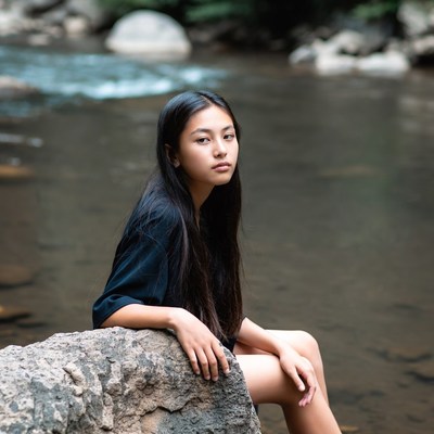 Asian girl sitting on rock by stream