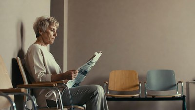 Elderly woman reading newspaper in waiting room