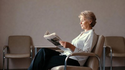 Elderly woman reading newspaper in waiting room