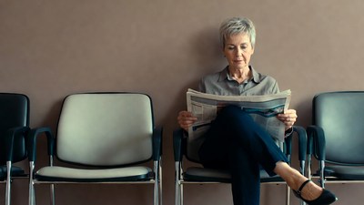 Elderly woman reading newspaper in waiting room